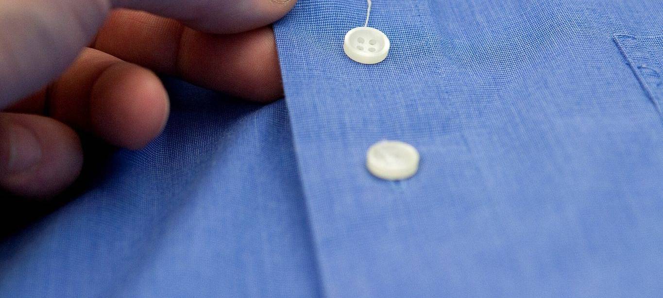 Bei einem Hemd hat sich am Knopf ein Faden gelöst