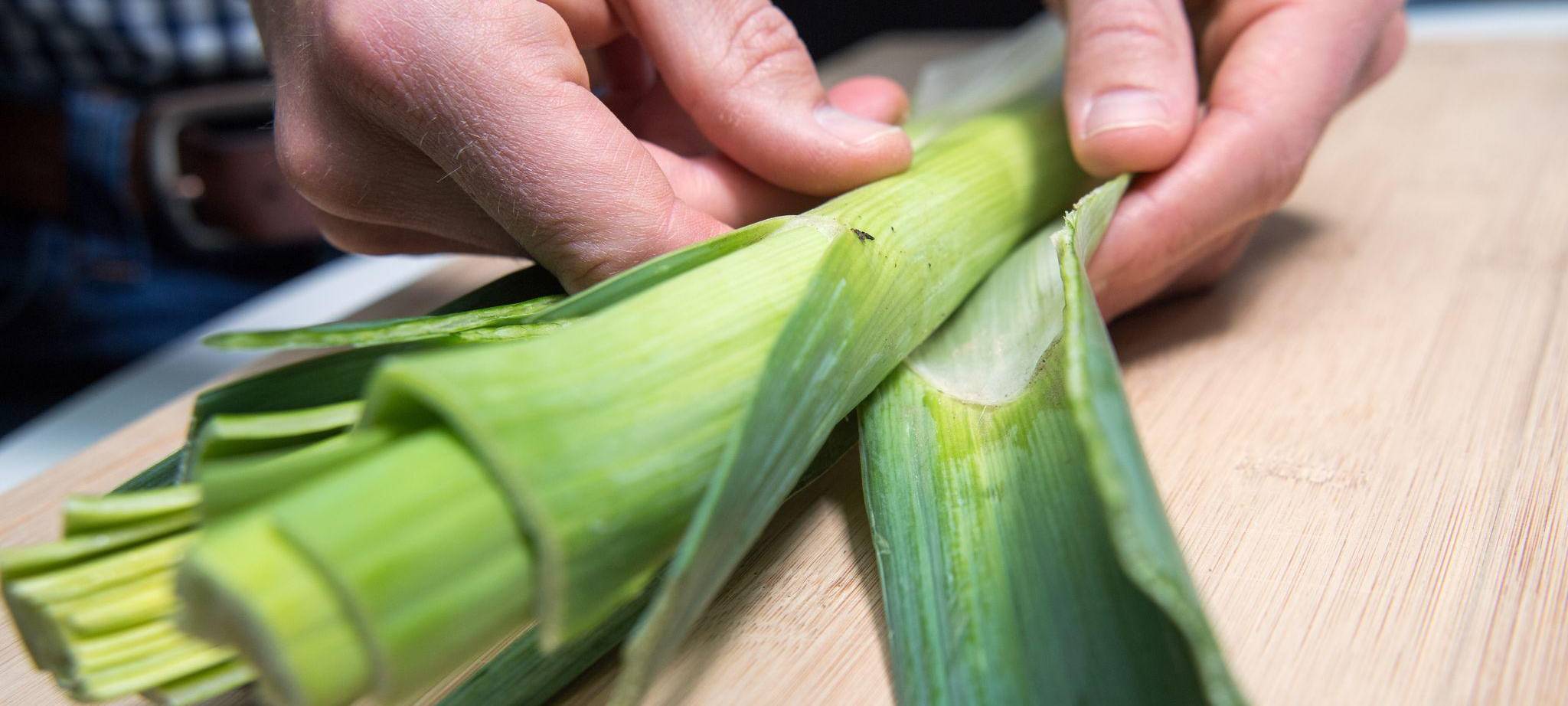 Mann entfernt die äußeren Blätter einer Lauchstange