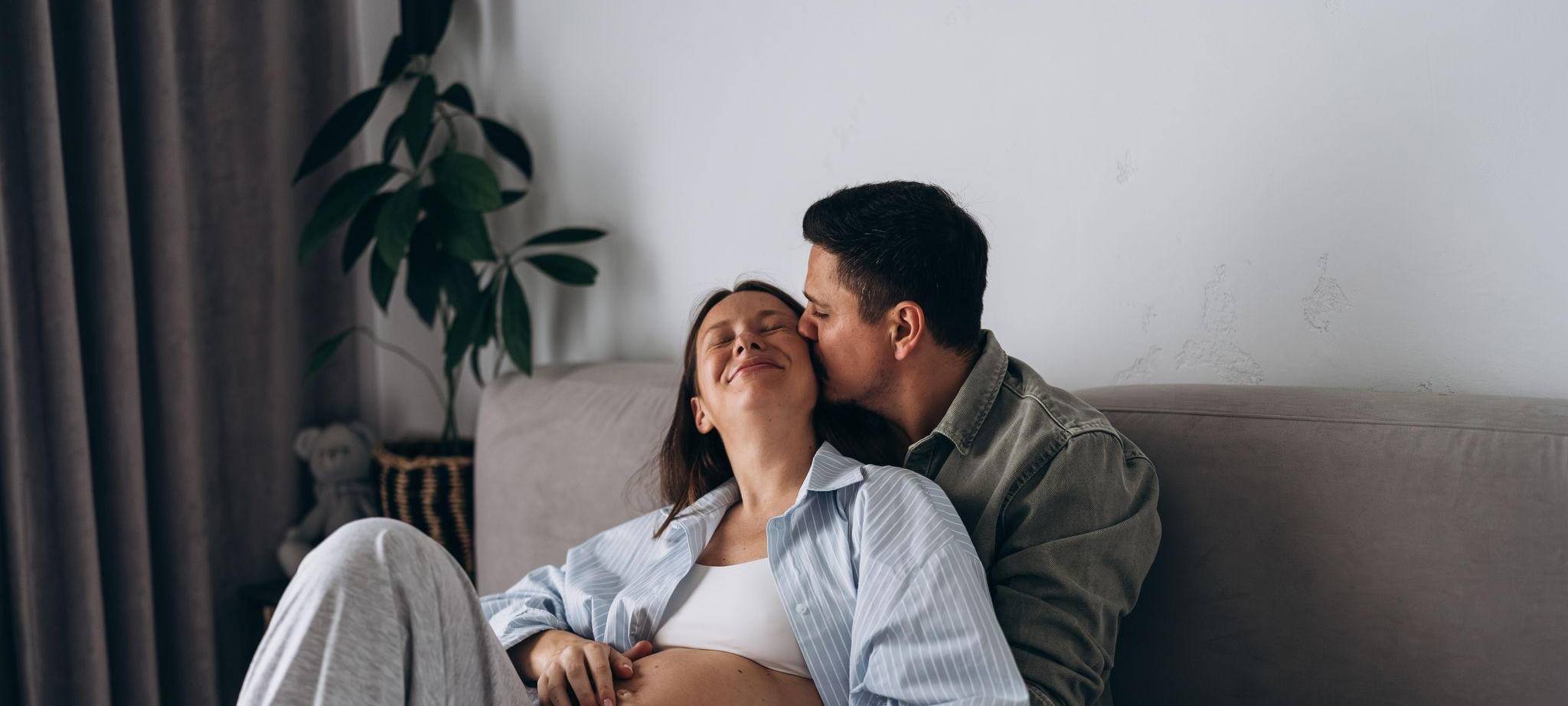 Eine schwangere Frau liegt mit ihrem Partner kuschelnd im Bett