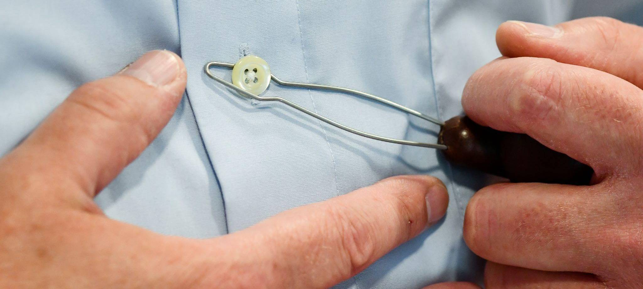 Mann nutzt eine Anziehhilfe, um den Knopf an einem Hemd zu öffnen