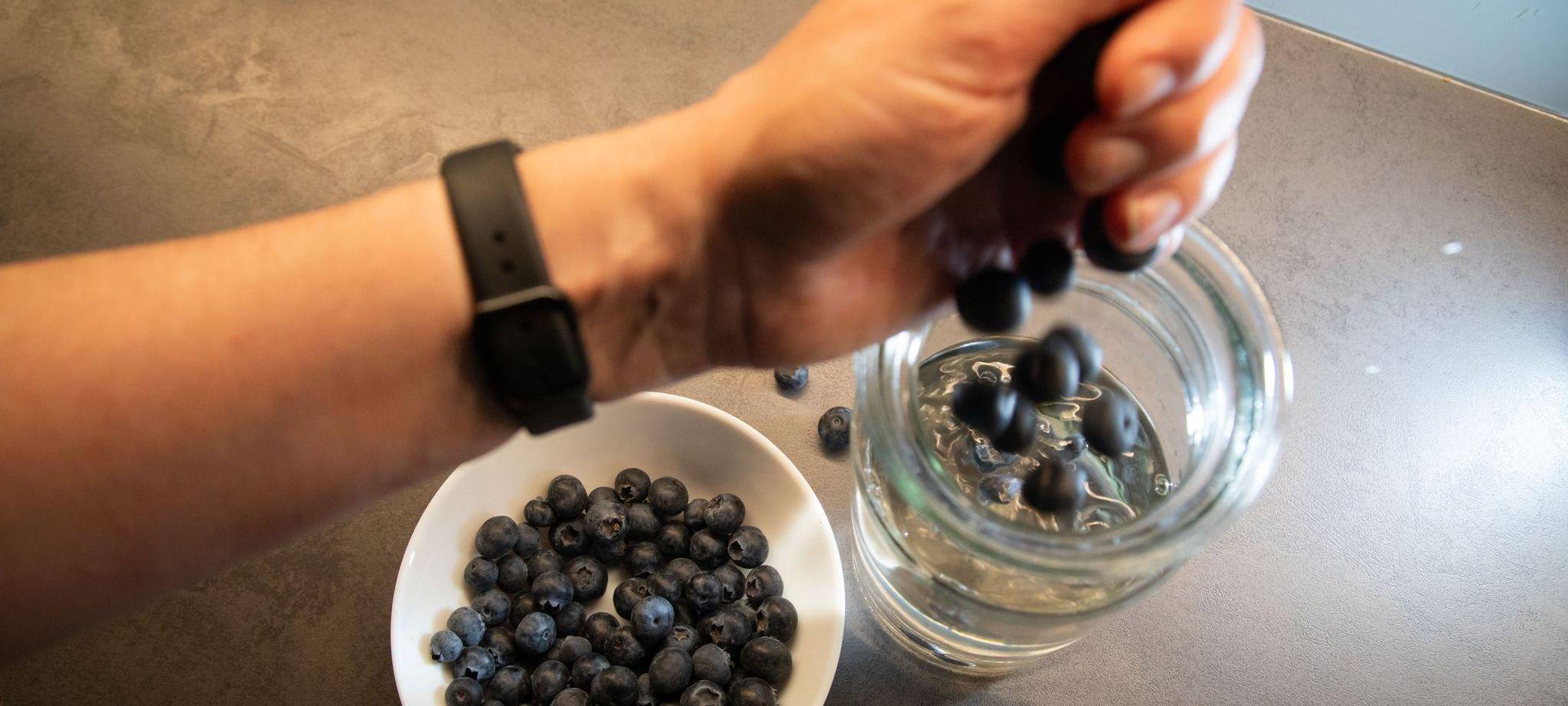Frau gibt Blaubeeren in ein Glas mit Wasser