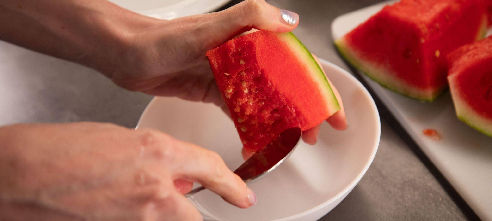 Frau schabt Kerne einer Wassermelone aus dem Fruchtfleisch