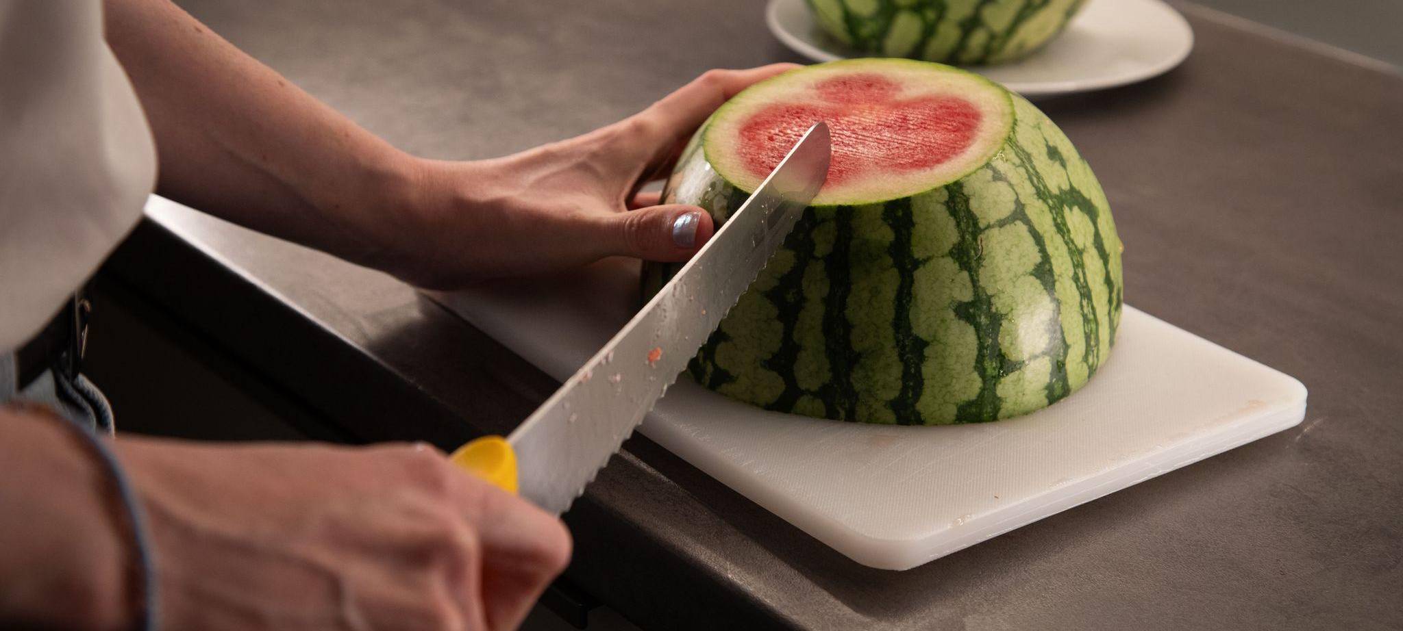 Frau schneidet die Schale einer aufgeschnittene Wassermelone an