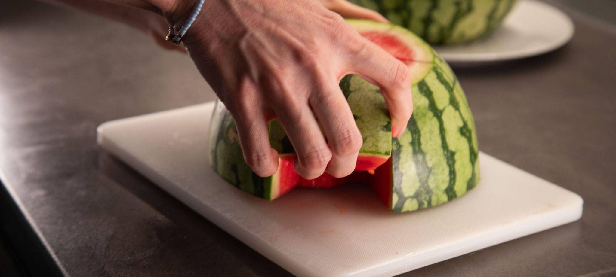 Frau schneidet Stücke aus einer Wassermelone heraus