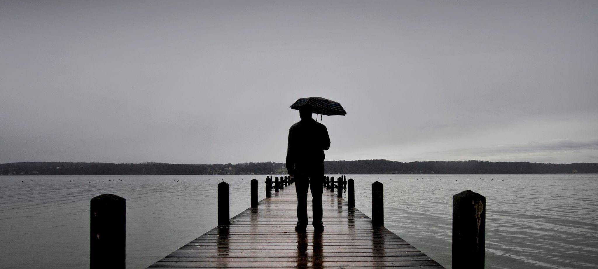 Ein Mann steht mit einem Regenschirm auf einem Steg