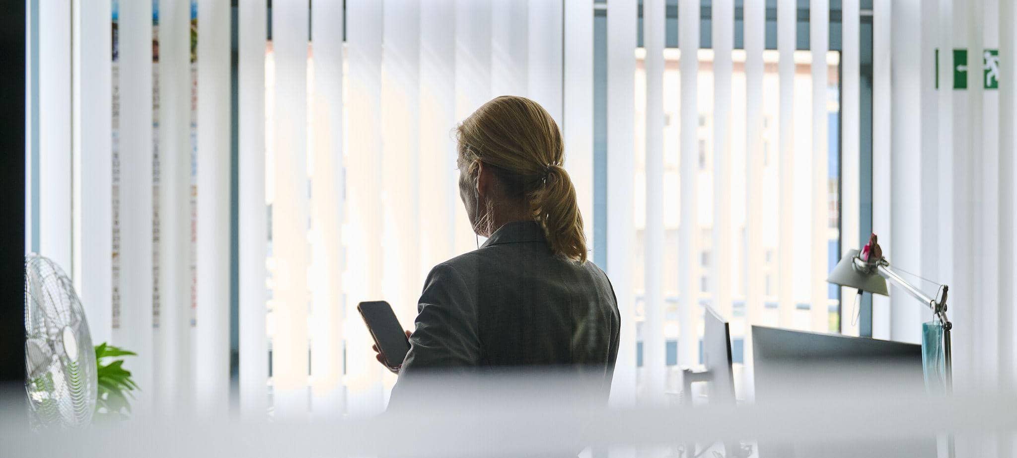 Frau steht in einem Bürozimmer am Fenster und telefoniert